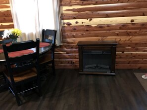 A wooden cabin interior with a dining table, chairs, and a fireplace.