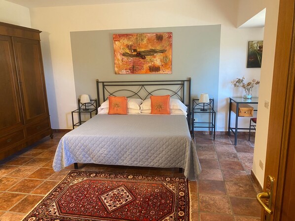 A bedroom with a bed, two nightstands, a wooden wardrobe, a painting, and a desk with a vase. - Casa Vacanze Etrusco – Leccio Apartment (San Gimignano)