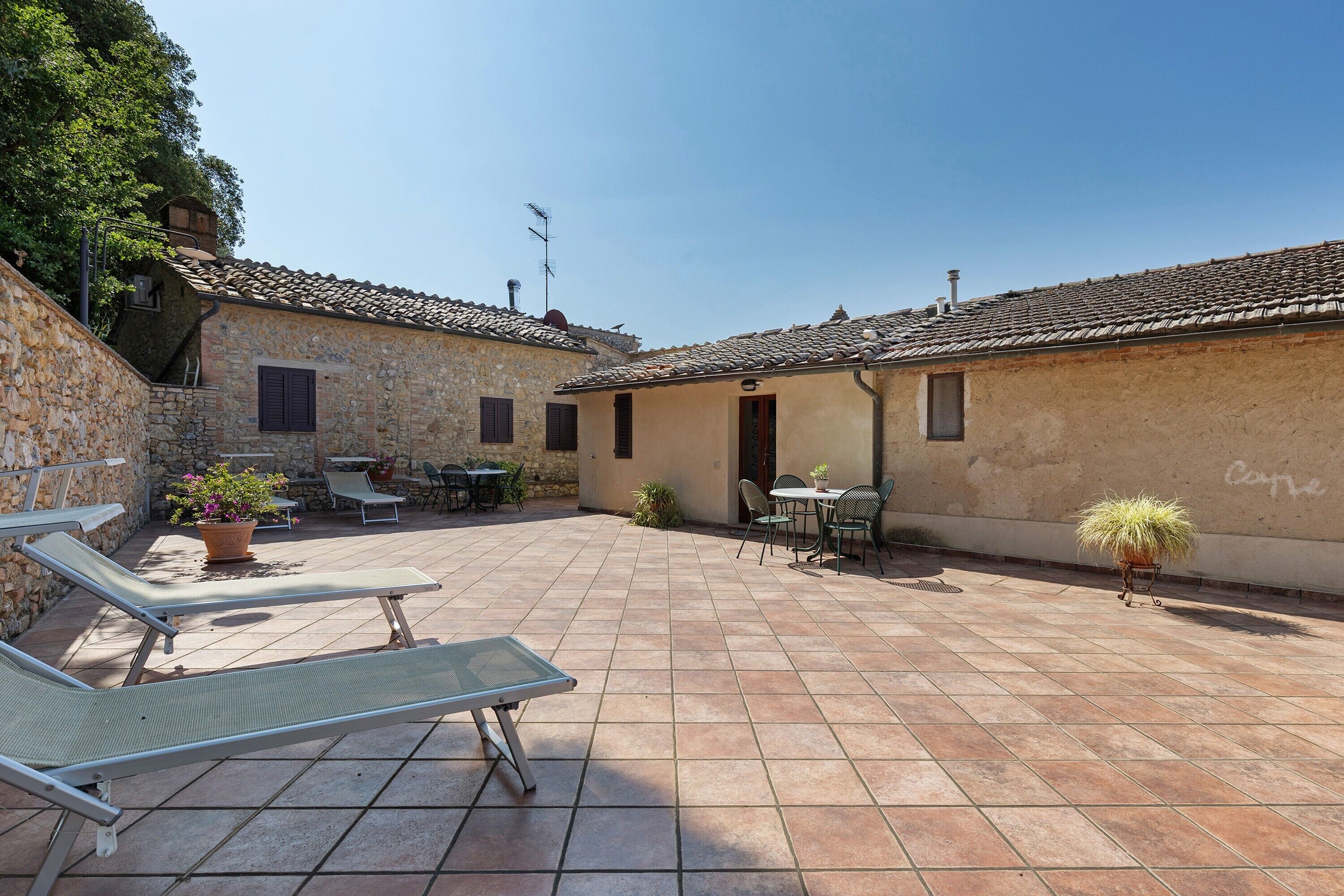 A courtyard with stone walls, tiled flooring, outdoor furniture, and potted plants.