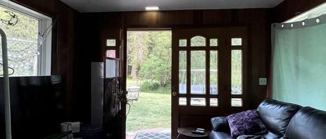 Una habitación compacta con sofá, una mesita, un banco, una puerta que da al exterior y un ventilador de techo.