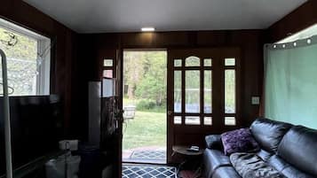 Una habitación compacta con sofá, una mesita, un banco, una puerta que da al exterior y un ventilador de techo.
