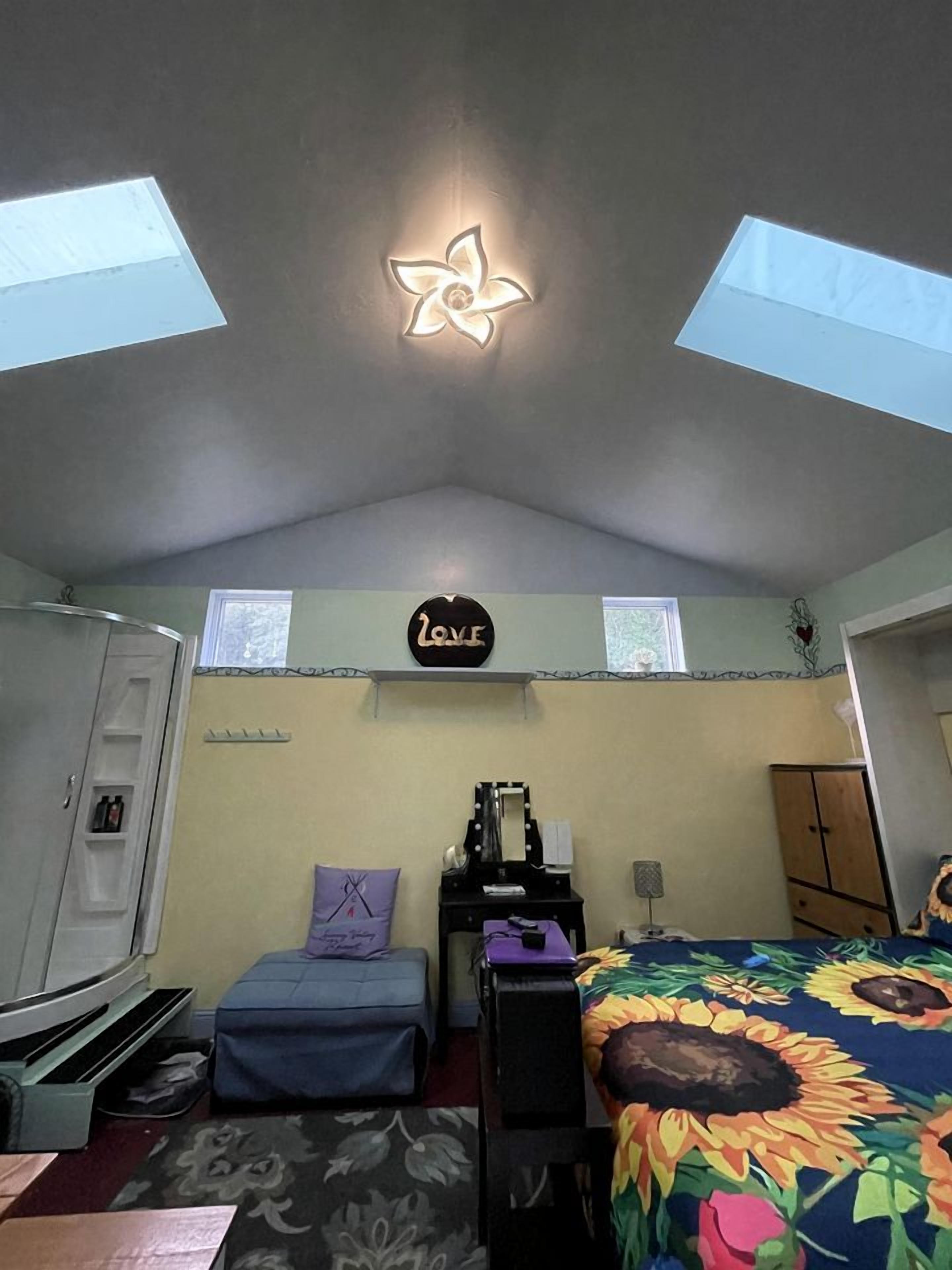 A bedroom with skylights, a bed with a floral bedspread, a desk with a mirror, a wardrobe, and a small window.