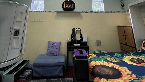 A bedroom with skylights, a bed with a floral bedspread, a desk with a mirror, a wardrobe, and a small window.
