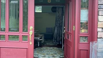 A red door with glass panels, a patterned mat, and a small figurine on the porch.