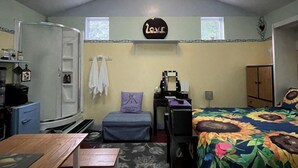 Une pièce compacte comprenant un lit, un bureau et une kitchenette. Elle est dotée de fenêtres de toit, d’un luminaire au plafond et d’une étagère murale ornée d’un panneau indiquant le mot « AMOUR ».