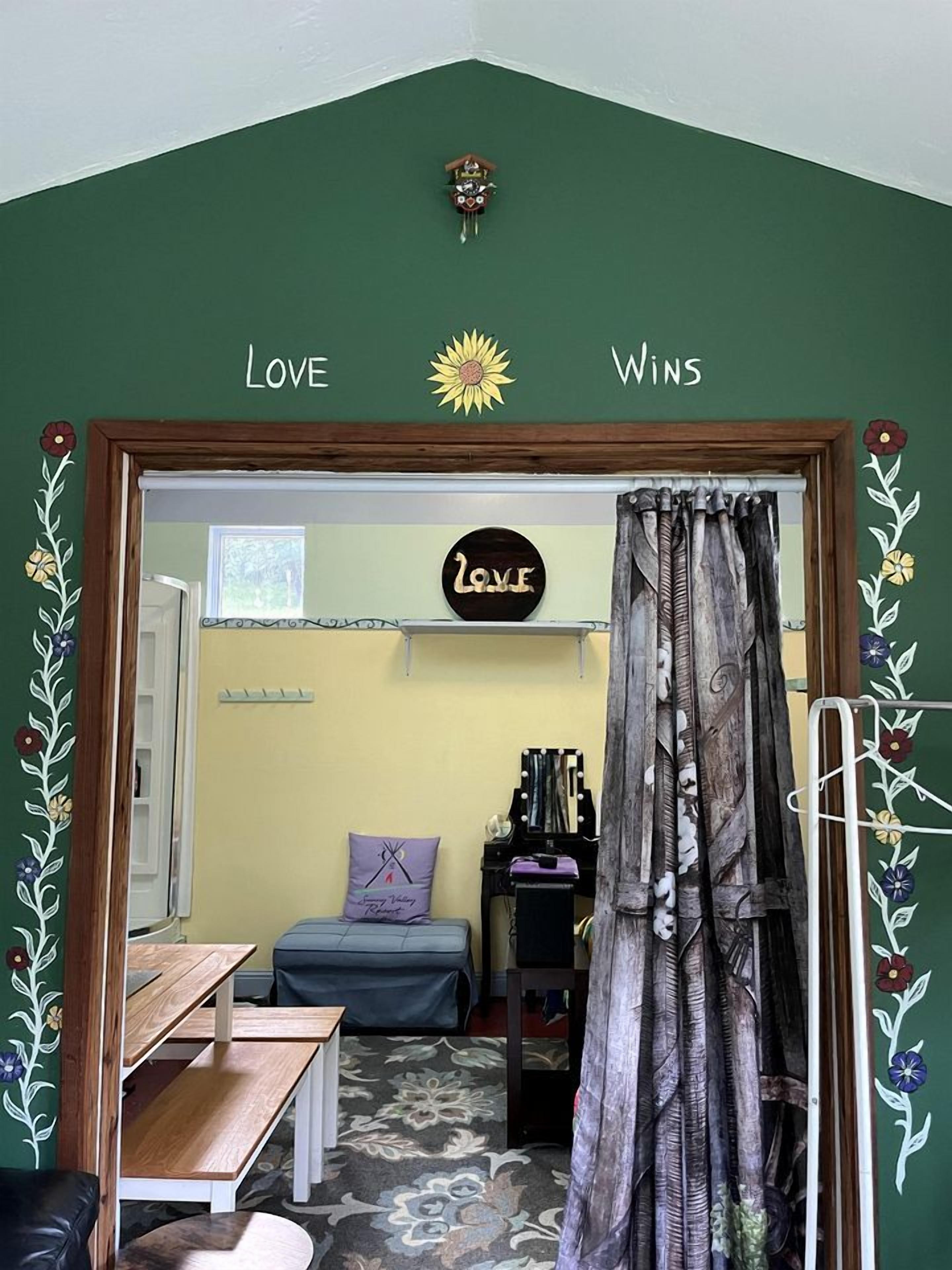 Una habitación con una pared verde, un banco de madera, una cama con un cojín púrpura y un cartel que dice 'LOVE'.