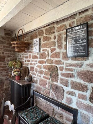 A stone wall with a signboard, a wicker basket, a framed picture, and a bench with floral cushions. - The pretty red sandstone house (Lagleygeolle)
