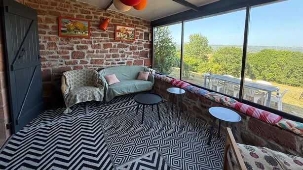 A room with a brick wall, a sofa, a patterned rug, and a view through large windows.