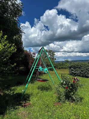 A swing set in a grassy area with trees and a cloudy sky.