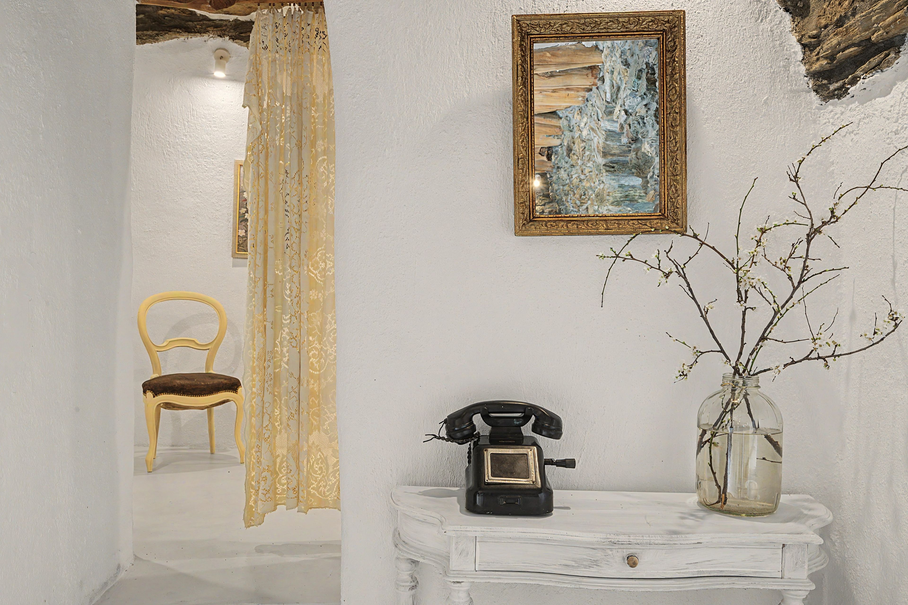 Een kamer met een witte muur, een lijst met schilderij, een telefoon en een vaas met takken.