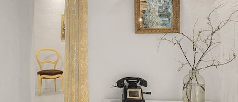 Une pièce avec un mur blanc, un tableau encadré, un téléphone et un vase orné de branches.