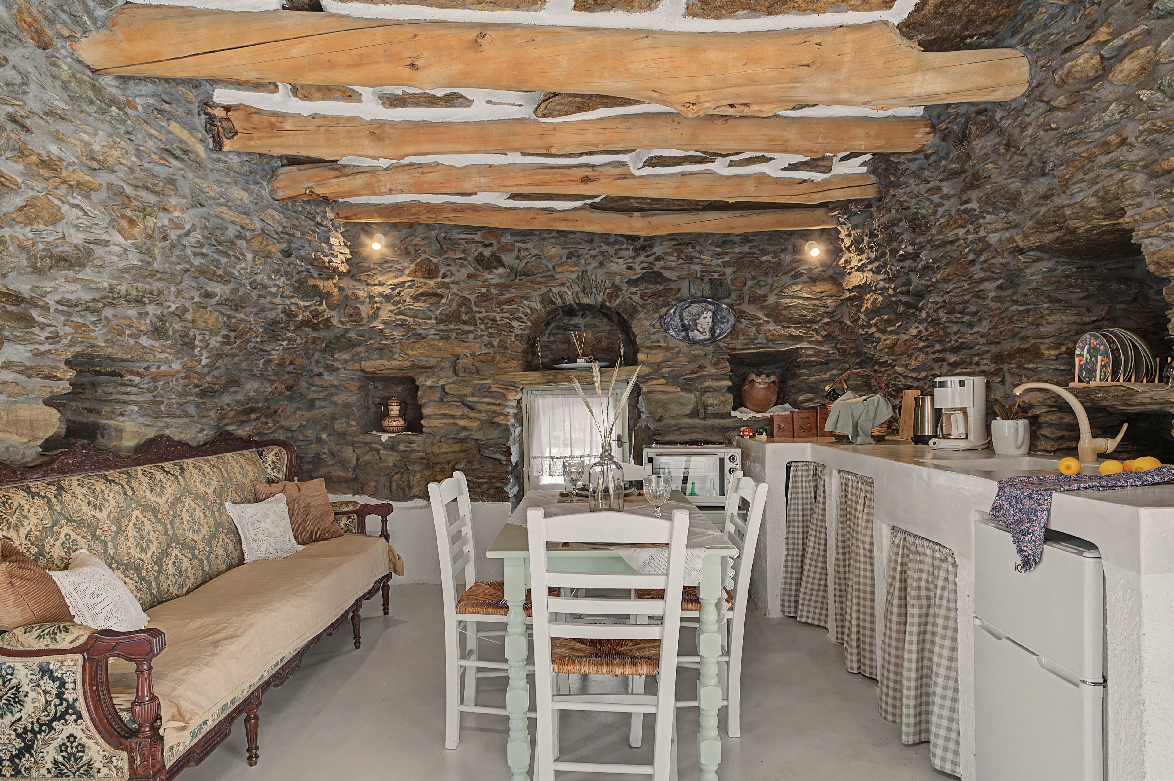 A rustic stone interior with a dining area, white furniture, and a stone fireplace.