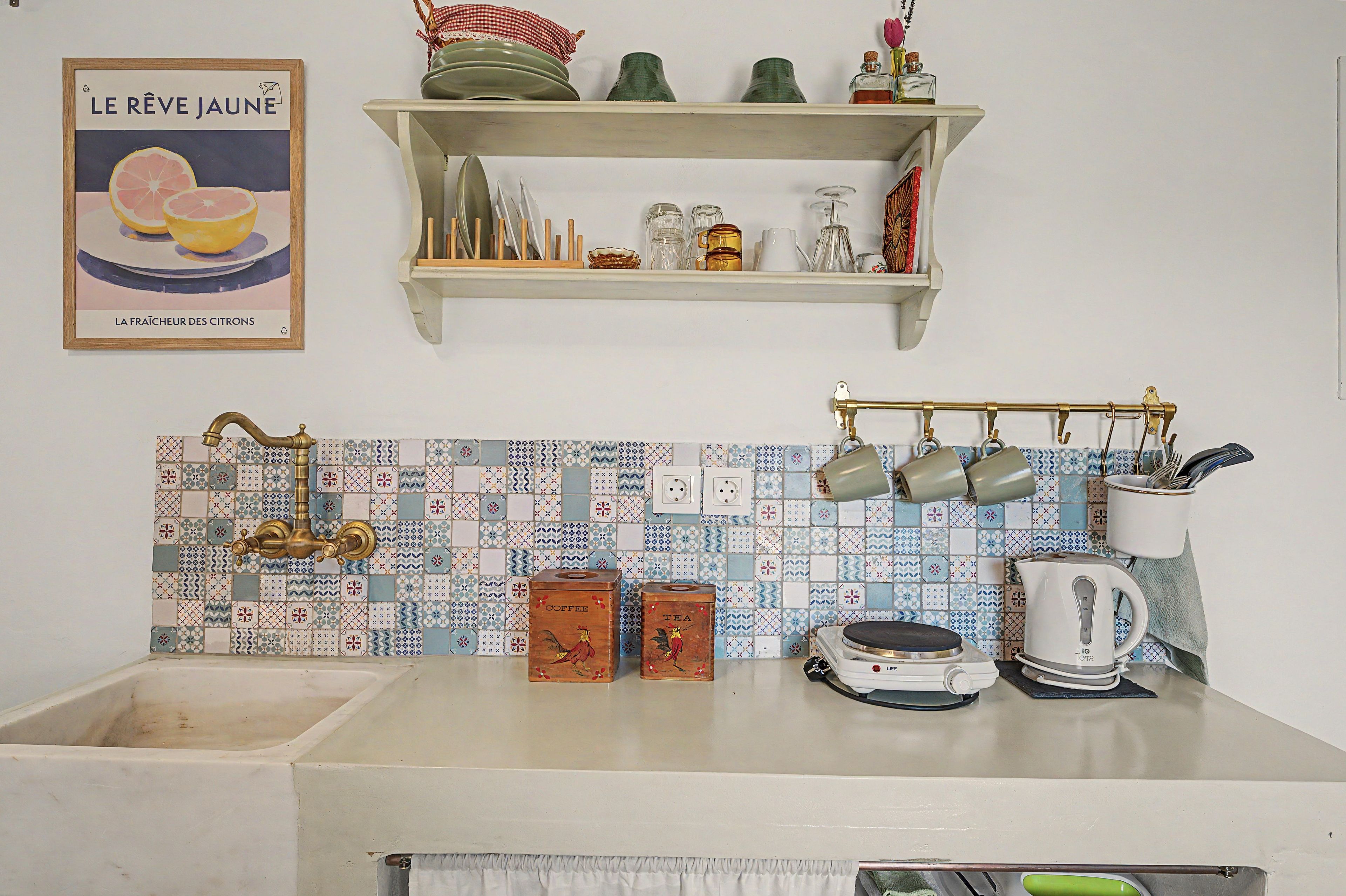 A kitchen with a tiled backsplash, a hanging pot rack, and a shelf above the sink.