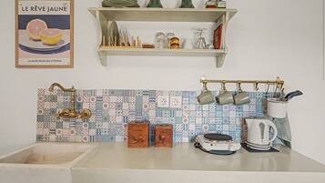 A kitchen with a tiled backsplash, a hanging pot rack, and a shelf above the sink.
