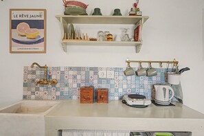 Una cocina con salpicadero de azulejos, un colgador para ollas y un estante sobre el fregadero.