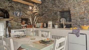 A rustic kitchen with stone walls, a dining table set for two, and a coffee machine.