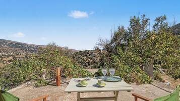 Un espace de restauration en plein air avec une table dressée pour deux personnes, entouré de verdure et avec des collines en arrière-plan.