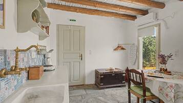 A rustic kitchen with a sink, wooden beams, a white door, and a window with a view of greenery.
