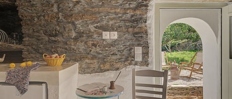 A stone wall, a wicker basket, a table with a book and a cup, and a chair with a woven seat.