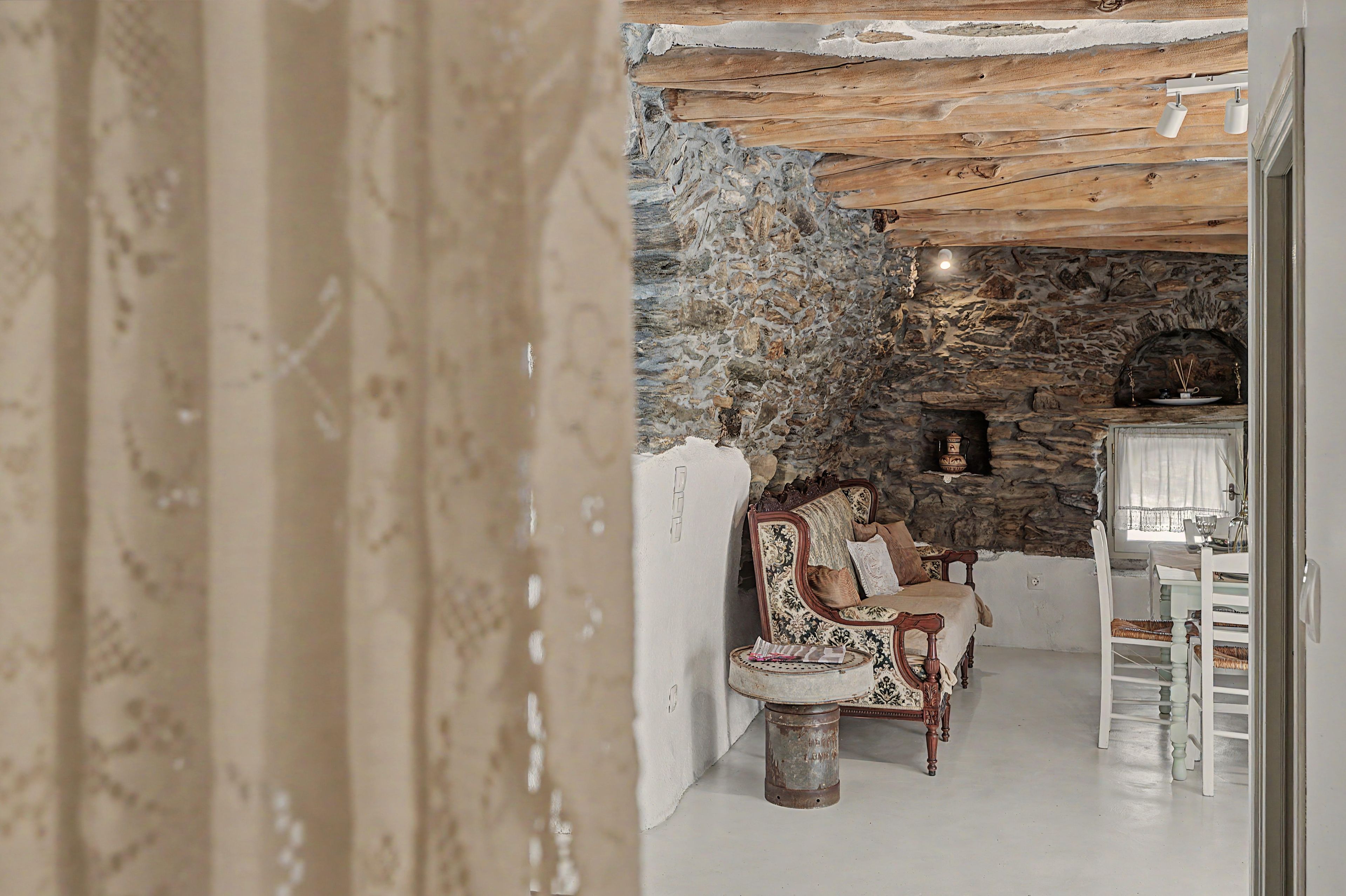 Ein rustikales Interieur mit einer Steinwand, einem Kamin und einer Sitzecke mit einem gemusterten Sessel und einem kleinen Tisch.