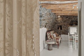 A rustic interior with a stone wall, a fireplace, and a seating area with a patterned armchair and a small table.