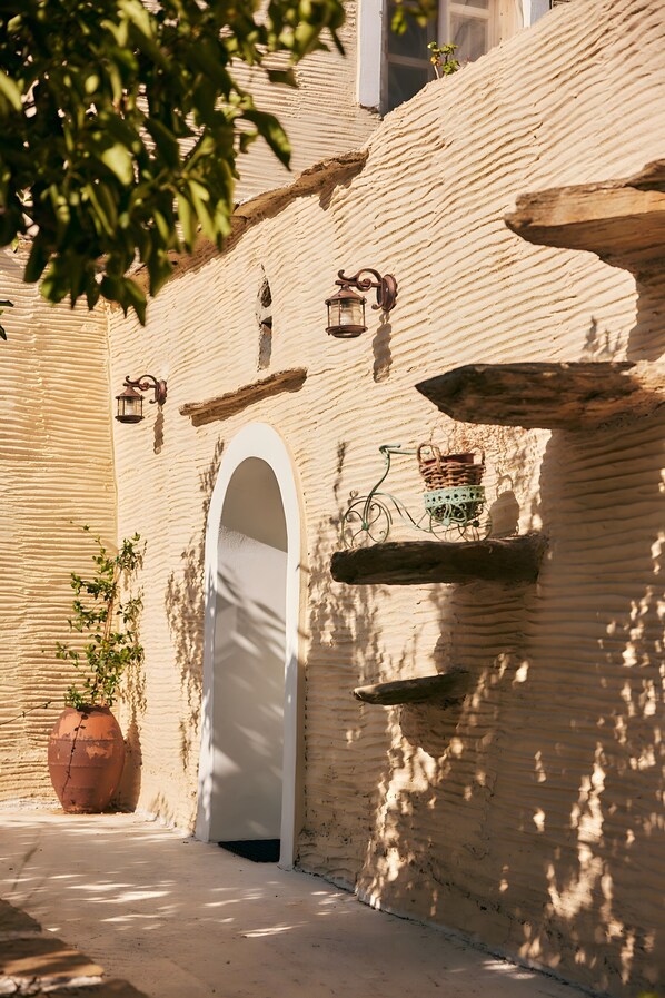A narrow alleyway with a white arched doorway, a wall-mounted lantern, and a wicker basket on a shelf.