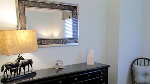 A black dresser with drawers, a mirror with ornate frame, a lamp, and a small clock.