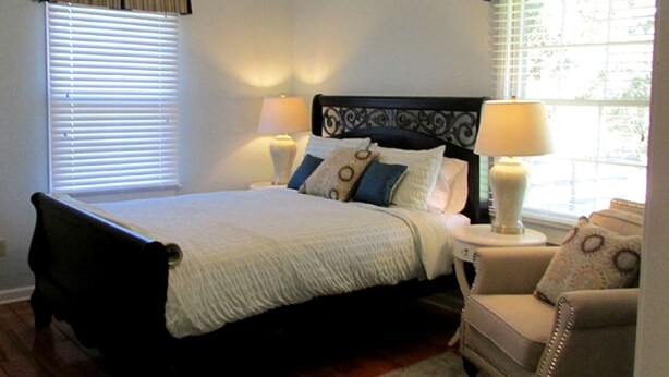 A bedroom with a bed, two bedside lamps, a chair, and a window with curtains.