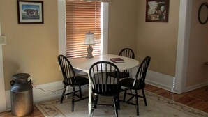 A dining area with a round table, four chairs, a lamp, and two framed pictures on the walls.