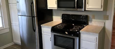 Una cocina con electrodomésticos de acero inoxidable, armarios blancos y piso de baldosas.
