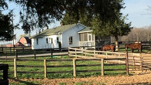 A stable with horses, a white house, and a barn in the background.