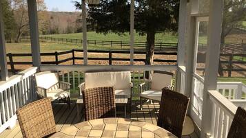 A covered outdoor seating area with wicker chairs and a table, overlooking a fenced pasture.
