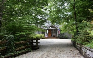A house with a gravel driveway, surrounded by dense greenery and a wooden fence. - Amazing Cottage with Fire Pit and Hot-tub in Lake Santeetlah, North Carolina (Lake Santeetlah)