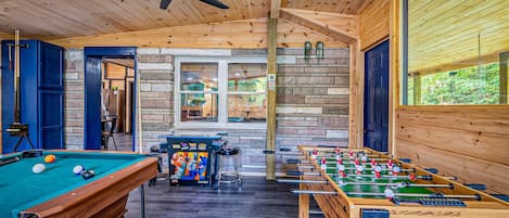 Una habitación con suelo de madera, mesa de billar, mesa de fútbol de mesa y mesa de billard.