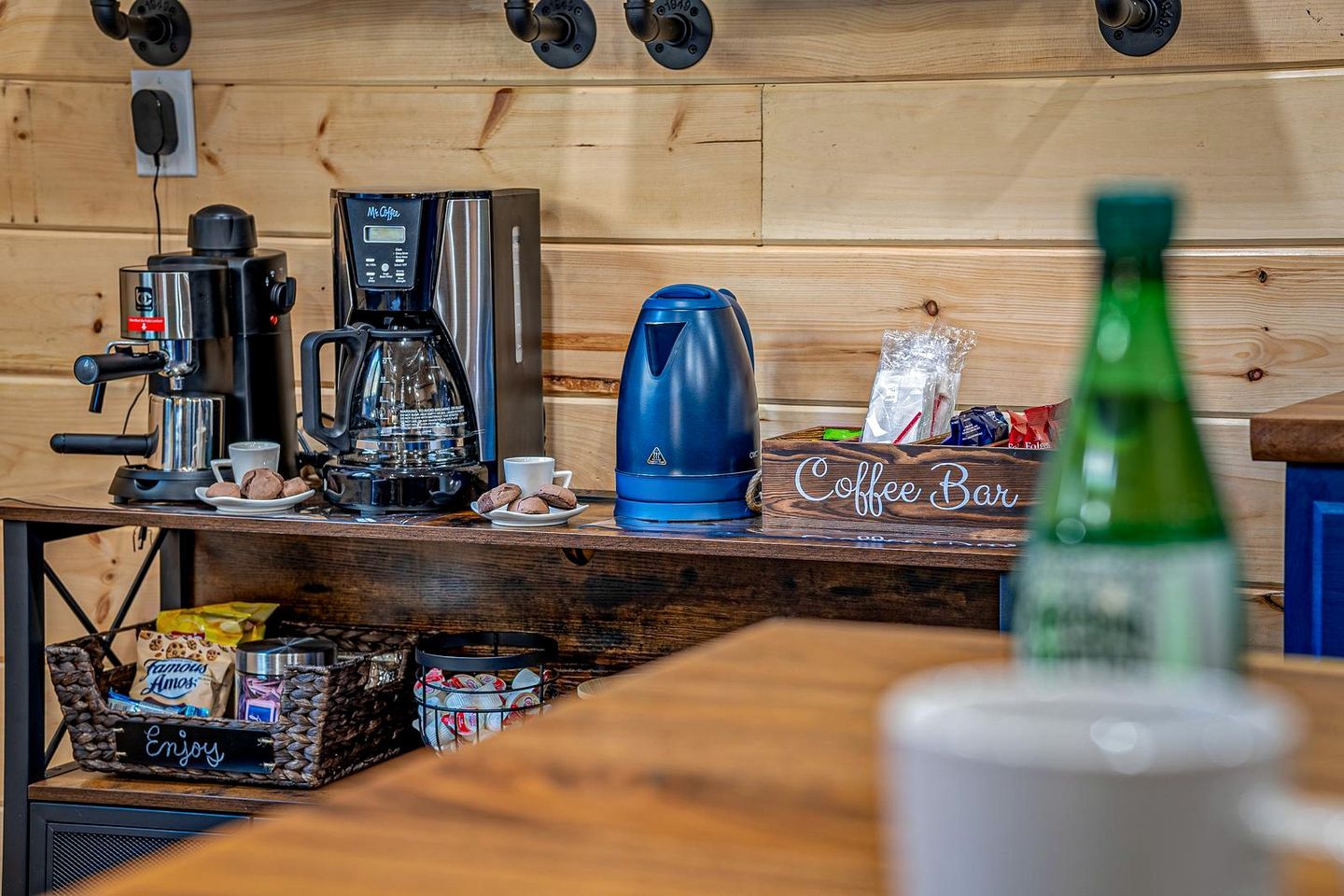 A coffee bar with a coffee machine, a kettle, and a coffee urn on a wooden counter.