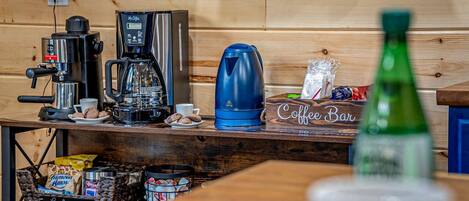 A coffee bar with a coffee machine, a kettle, and a coffee urn on a wooden counter.