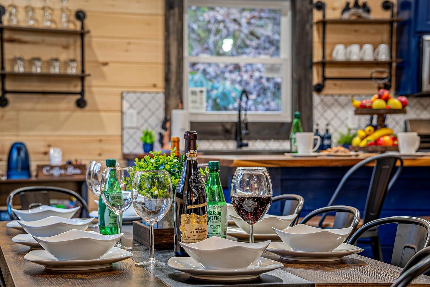 Een eettafel gedekt met witte borden, kommen en glazen, met wijnflessen en een champagnefles.