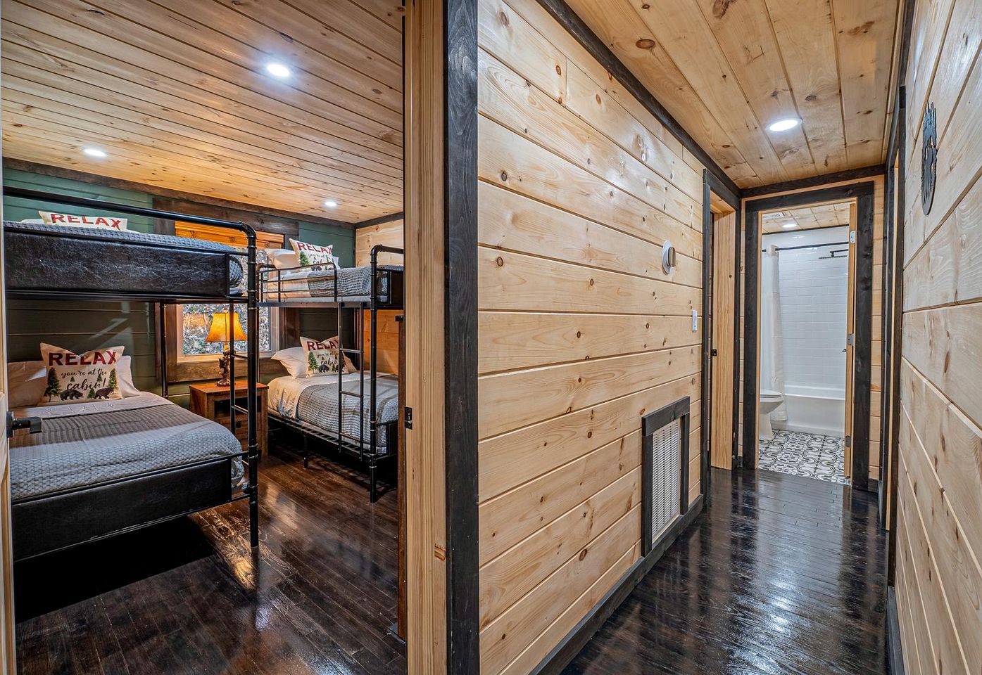 A bunk room with wooden walls and a wooden floor, a bathroom with a shower, and a hallway with a door.