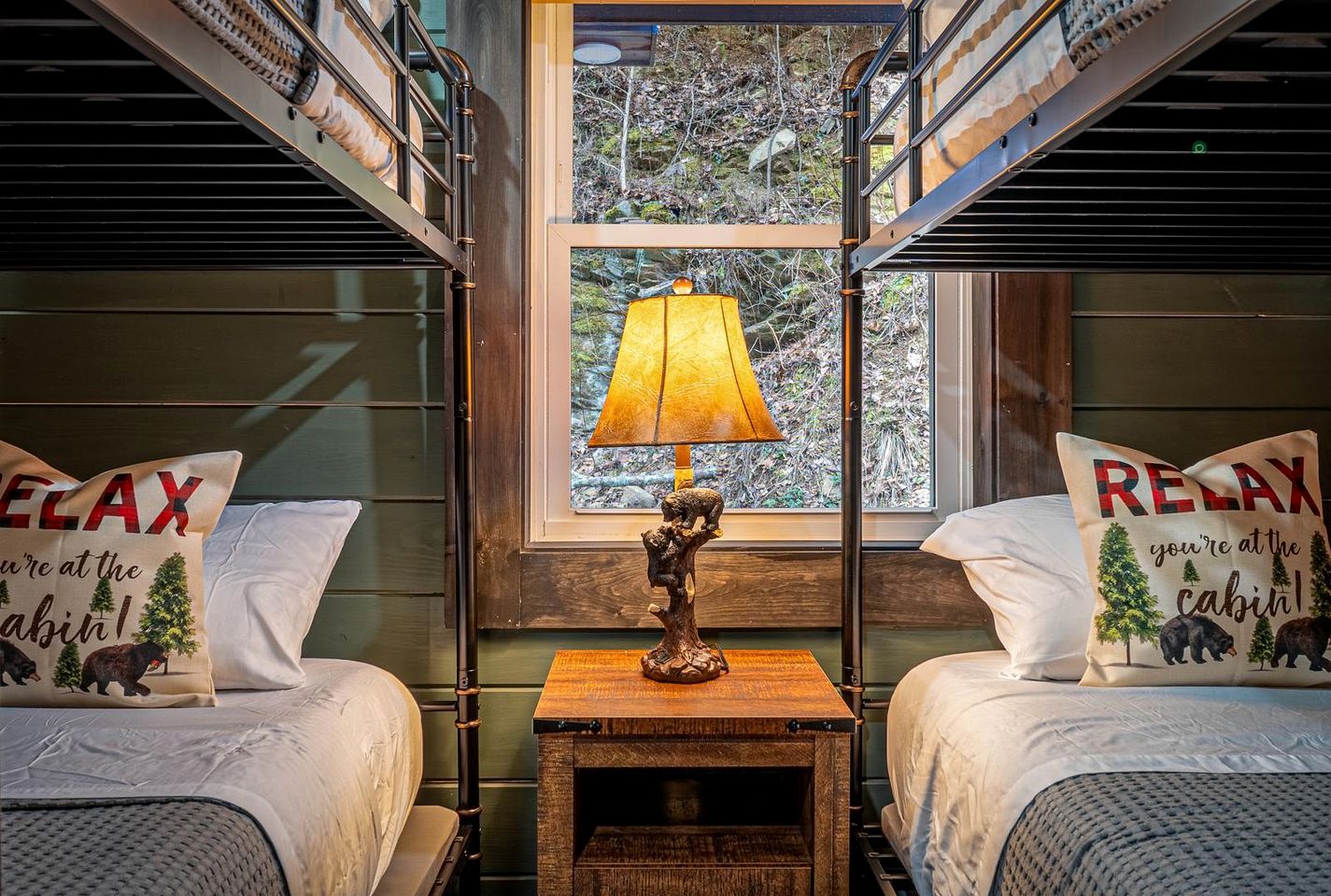 Ein Blockhaus-Interieur mit zwei Betten, einer Lampe und einem Fenster mit Blick auf Bäume.