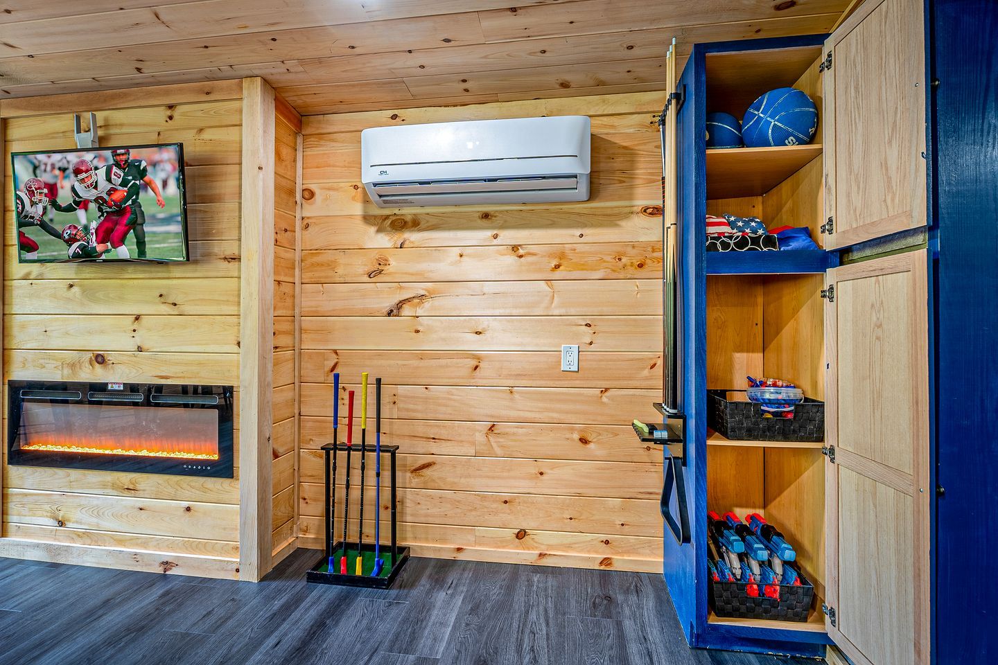 A wooden cabin interior with a fireplace, an air conditioning unit, a television, and a storage cabinet.