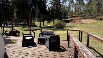 A wooden deck with outdoor furniture, a grill, and a view of a forested area.