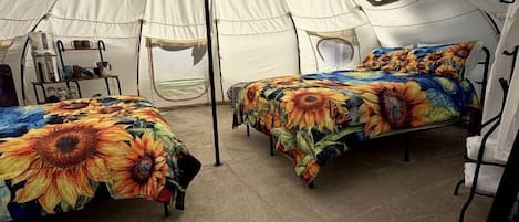 A tent with two beds, each with a sunflower-patterned bedspread, and a central pole.