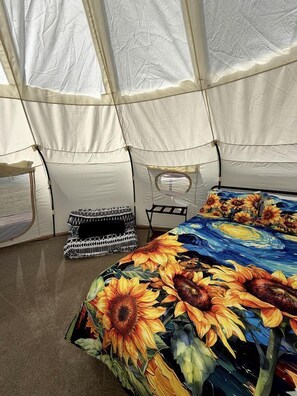 Ein Zelt mit einem Bett, das einen Sonnenblumenmuster-Druck hat, einem schwarz-weißen Kissen und einem kleinen Tisch.