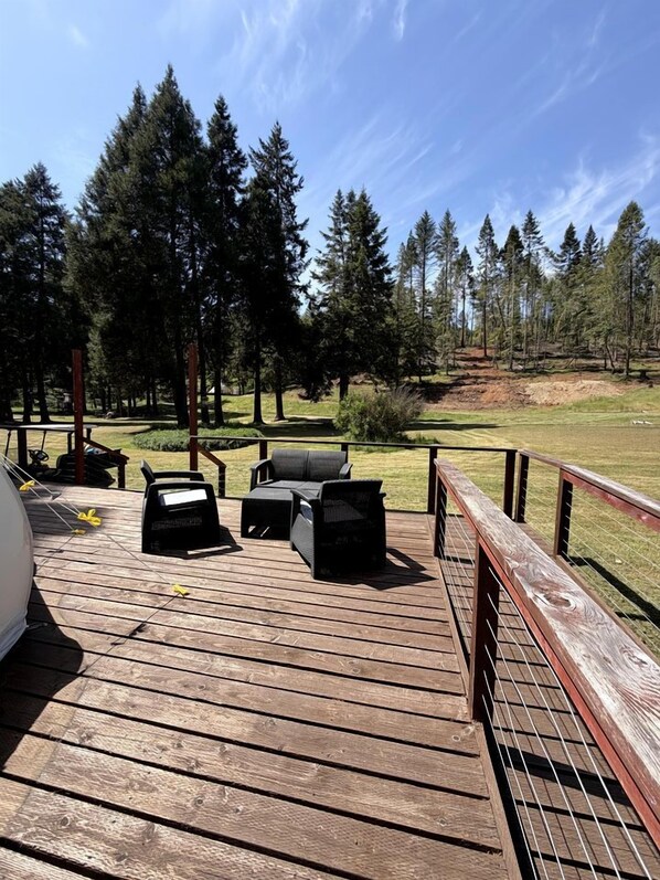 A wooden deck with outdoor furniture, a grill, and a view of a forested area.