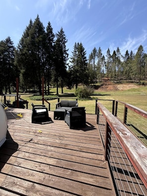 Une terrasse en bois avec des meubles d’extérieur, un barbecue et une vue sur une zone boisée.