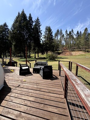 A wooden deck with outdoor furniture, a grill, and a view of a forested area.