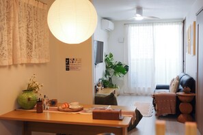 Ein Wohnzimmer mit einer Couch, einem Couchtisch, einem Fernseher und einem großen Fenster mit Vorhängen.