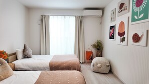 Ein Hotelzimmer mit zwei Betten, einem Fenster mit Vorhängen, Wandbildern und einem kleinen Tisch mit Blumenvase.