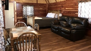 Interno di una baita di legno con tavolo da pranzo, sedie, divano, letto e ventola a soffitto.