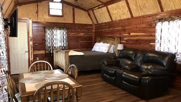 Interior de una cabaña de madera con una mesa de comedor, sillas, un sofá, una cama y un ventilador de techo.